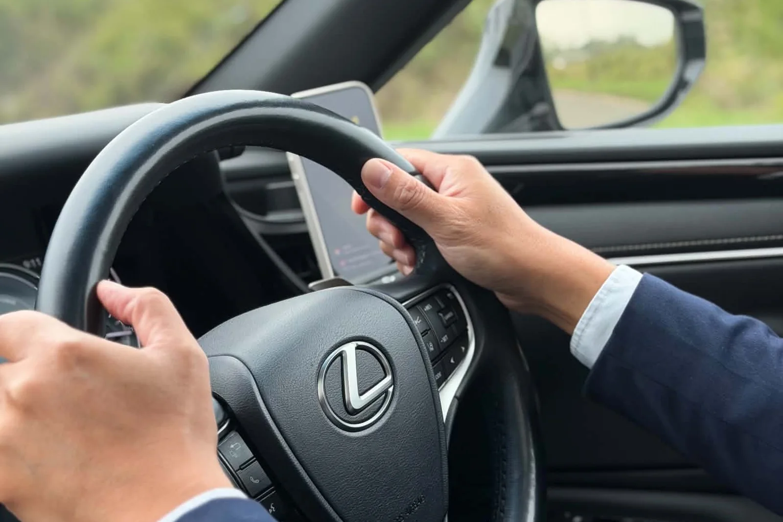 A Beyond Elite Travel chauffeur in a navy suit at the wheel of the Lexus ES